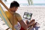 一个人坐在沙滩上用笔记本电脑看四个监控摄像头的画面.